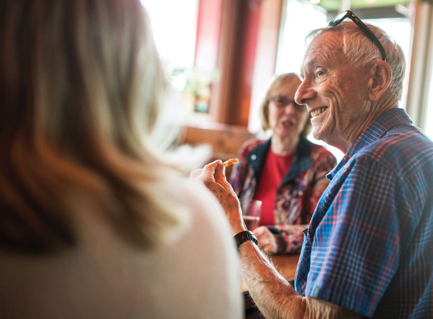 Man with eyeglasses propped on head smiling while eating at a table with others